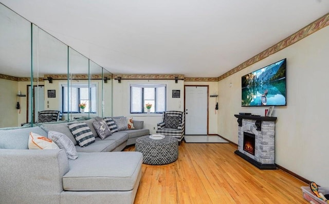 living room featuring baseboards, a stone fireplace, and light wood-style flooring