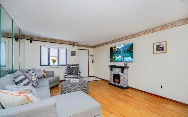 living room with baseboards, a stone fireplace, and light wood-type flooring
