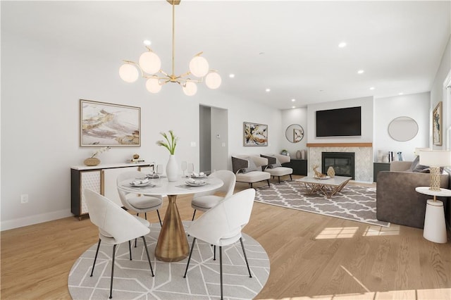 dining space featuring light wood-style floors, a chandelier, recessed lighting, baseboards, and a fireplace with flush hearth