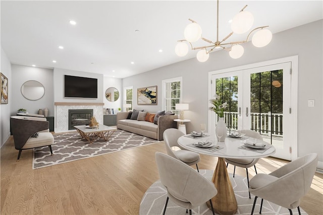 dining room featuring french doors, a high end fireplace, an inviting chandelier, recessed lighting, and light wood-style flooring