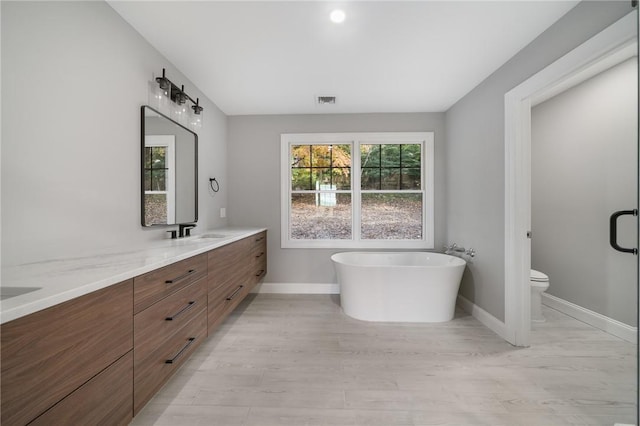 bathroom with visible vents, double vanity, toilet, baseboards, and a sink