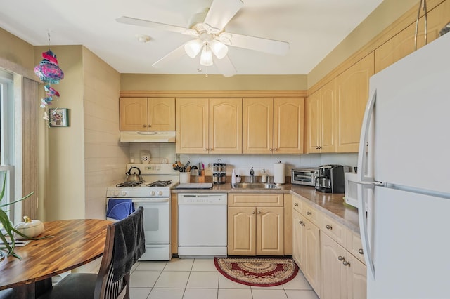 kitchen featuring white appliances, light brown cabinetry, under cabinet range hood, and a sink