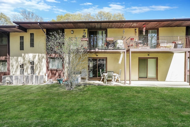 rear view of property featuring a lawn, stucco siding, and a balcony