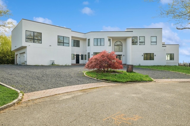 art deco home featuring gravel driveway, a garage, and stucco siding