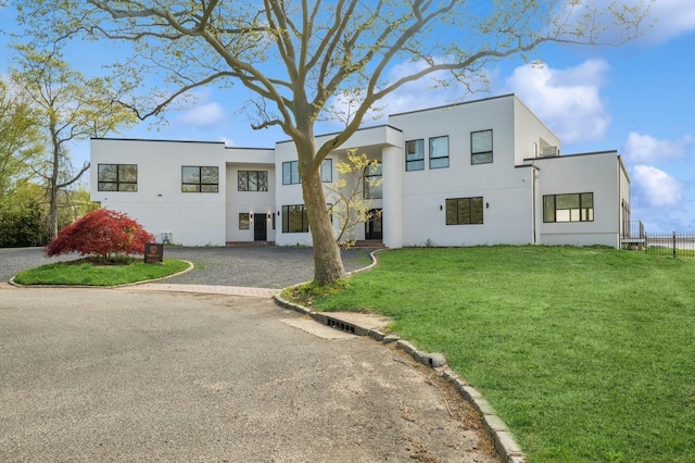 view of front of home featuring fence, stucco siding, gravel driveway, and a front yard