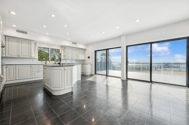 kitchen with visible vents, a water view, granite finish floor, and glass insert cabinets