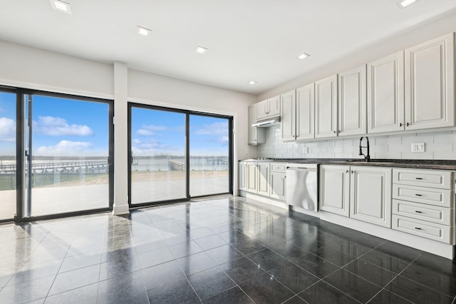 kitchen with stainless steel dishwasher, dark countertops, a sink, backsplash, and granite finish floor