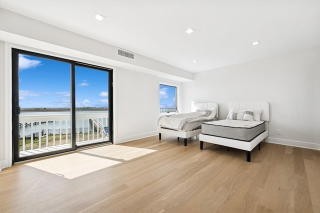 bedroom with visible vents, baseboards, light wood finished floors, a water view, and access to outside