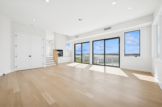 unfurnished living room with visible vents, light wood-style floors, baseboards, stairway, and recessed lighting