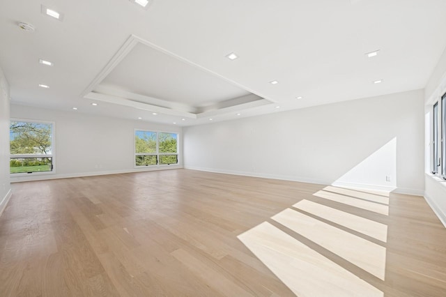 unfurnished living room featuring baseboards, light wood finished floors, a tray ceiling, and a healthy amount of sunlight
