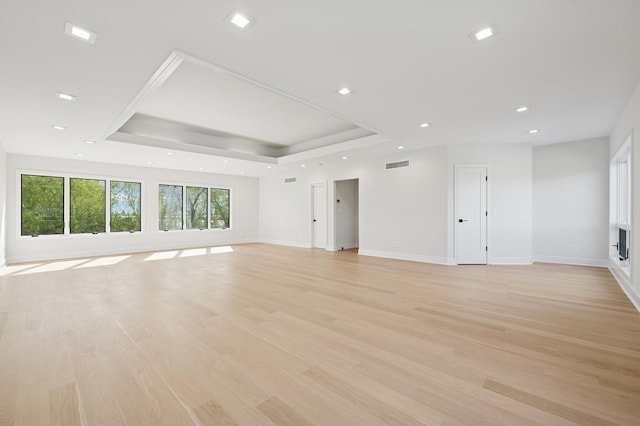 unfurnished living room with light wood finished floors, recessed lighting, baseboards, a tray ceiling, and visible vents