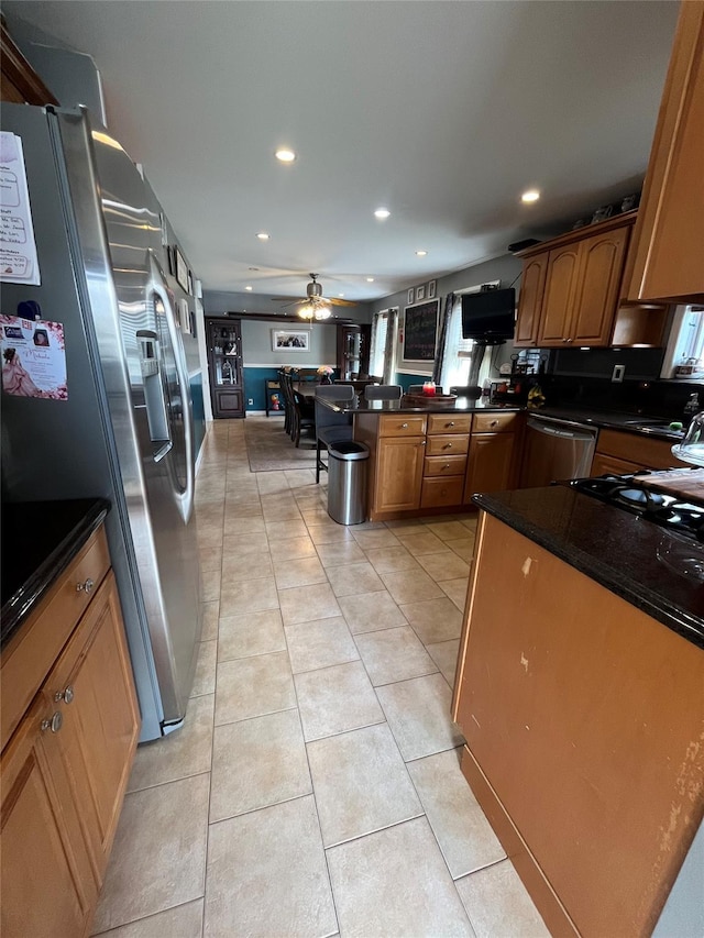 kitchen with a ceiling fan, a peninsula, dark countertops, and stainless steel appliances