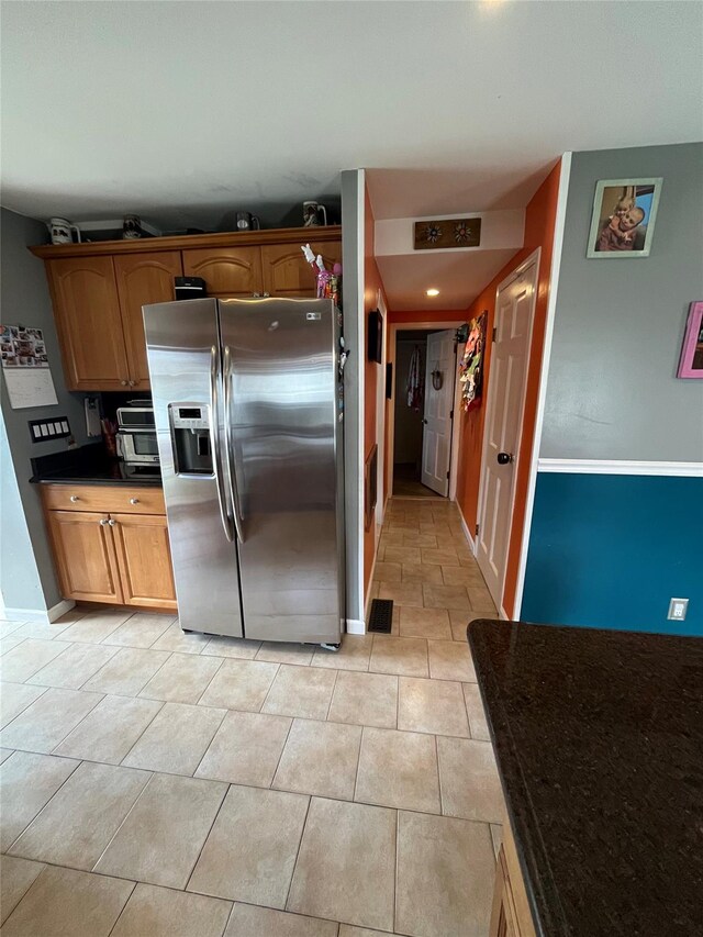 kitchen with visible vents, light tile patterned flooring, dark countertops, baseboards, and stainless steel fridge with ice dispenser