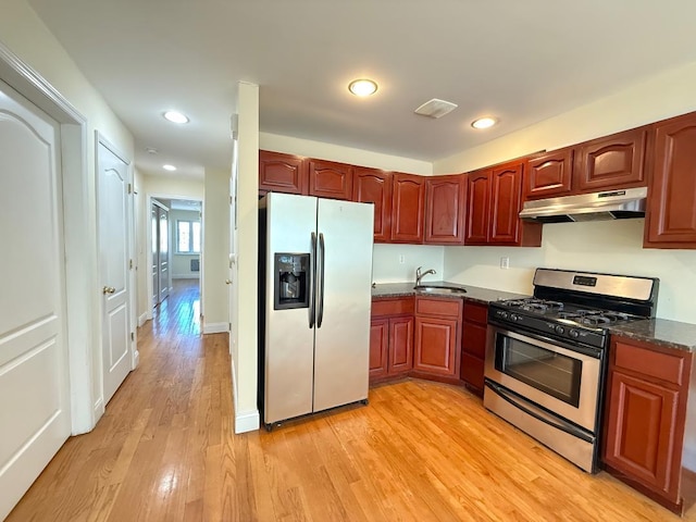 kitchen featuring a sink, dark stone counters, stainless steel appliances, light wood-type flooring, and under cabinet range hood