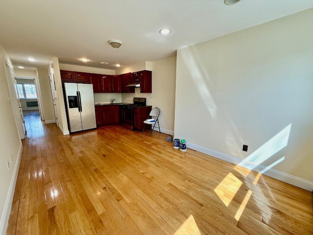 kitchen with gas range, fridge with ice dispenser, baseboards, reddish brown cabinets, and light wood-style floors