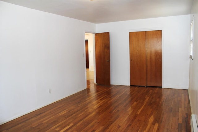 unfurnished bedroom featuring baseboard heating, wood finished floors, and a closet