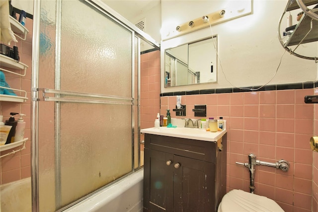 bathroom with tile walls, vanity, toilet, and shower / bath combination with glass door