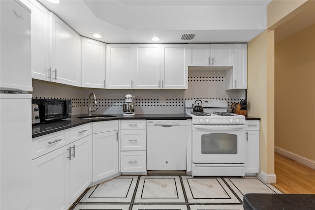 kitchen with visible vents, dark countertops, a sink, white appliances, and white cabinetry