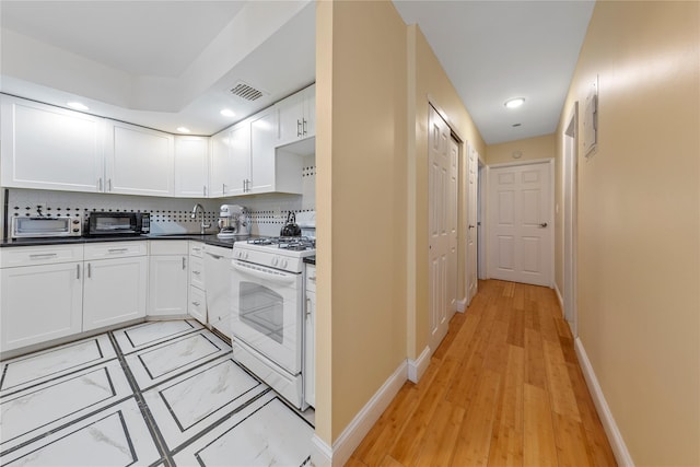kitchen with dark countertops, white appliances, white cabinetry, baseboards, and visible vents