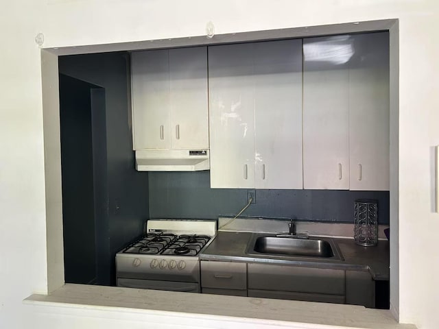 kitchen with under cabinet range hood, gray cabinets, range with gas stovetop, and a sink