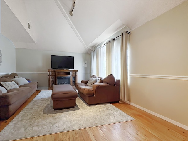 living room with a fireplace, wood finished floors, track lighting, baseboards, and lofted ceiling