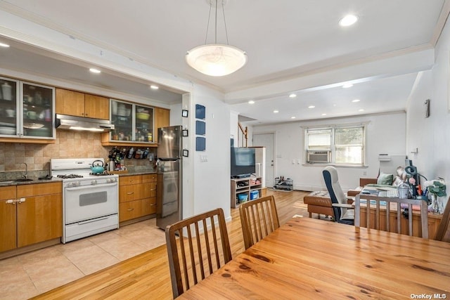 kitchen with tasteful backsplash, brown cabinets, white gas range oven, freestanding refrigerator, and under cabinet range hood
