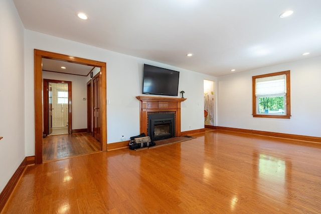 unfurnished living room featuring recessed lighting, baseboards, a fireplace with flush hearth, and wood finished floors
