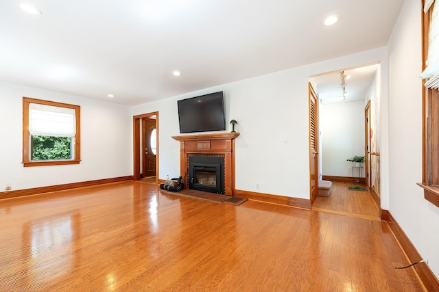 unfurnished living room featuring recessed lighting, light wood-style flooring, a glass covered fireplace, and baseboards
