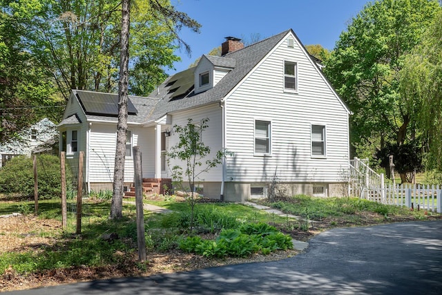 view of side of property featuring roof mounted solar panels, fence, a chimney, and roof with shingles