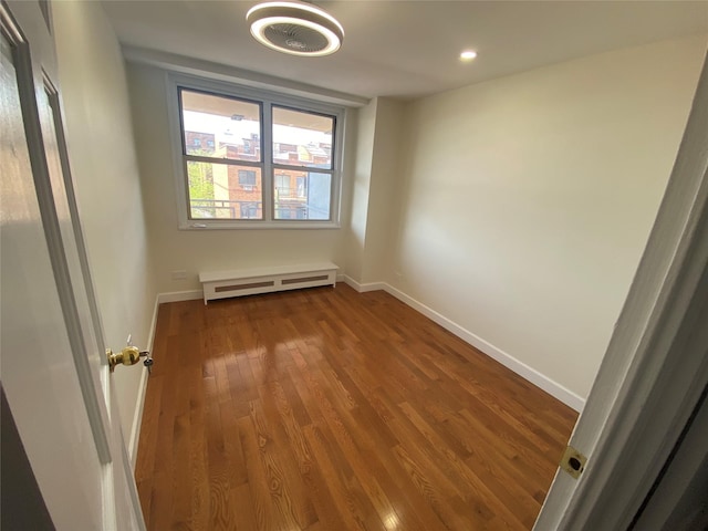 empty room featuring wood finished floors, recessed lighting, baseboards, and a baseboard heating unit