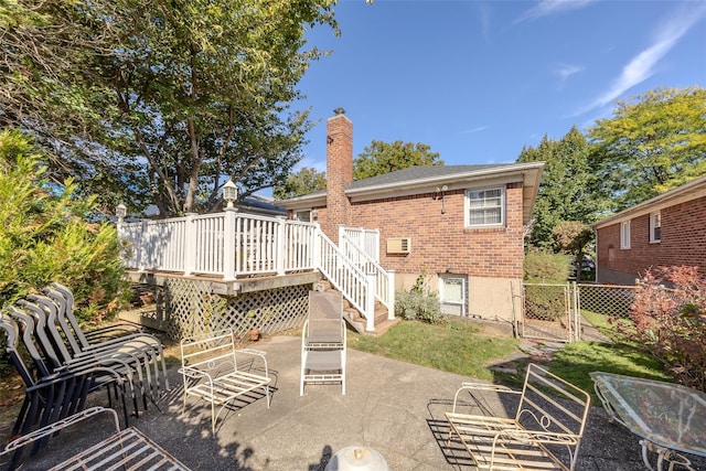 rear view of house featuring a chimney, a wooden deck, a gate, brick siding, and a patio