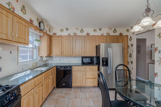 kitchen featuring dark stone counters, a sink, backsplash, black appliances, and hanging light fixtures