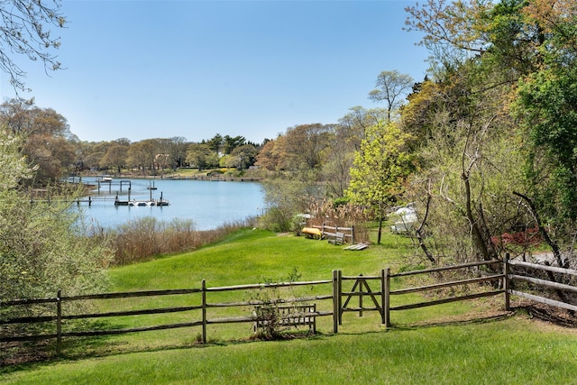 view of yard with a water view, fence, a boat dock, and a wooded view