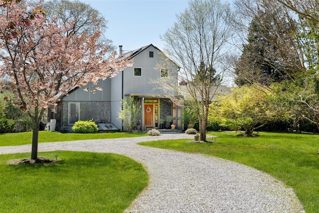 view of front facade with stone siding, curved driveway, and a front yard