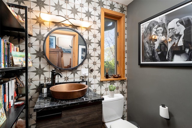 bathroom featuring a sink, backsplash, toilet, and tile walls