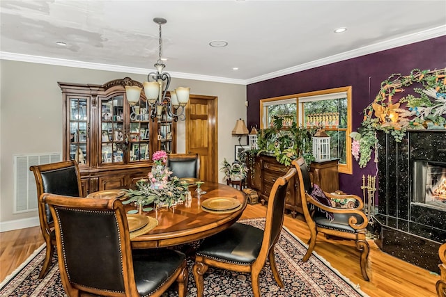 dining room with an inviting chandelier, wood finished floors, a fireplace, crown molding, and visible vents