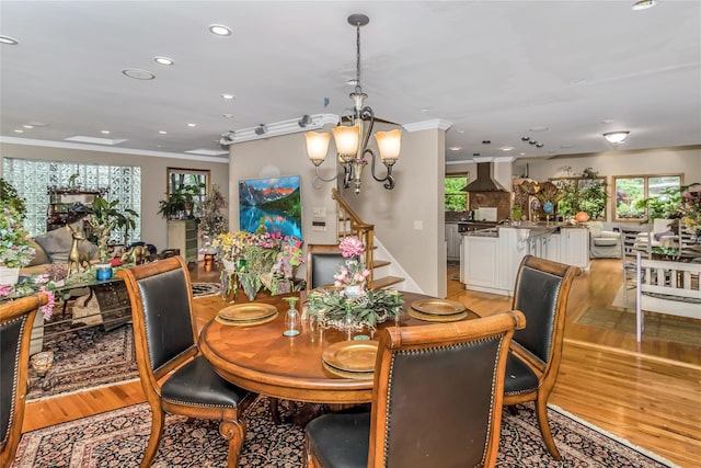 dining area with light wood finished floors, crown molding, and a notable chandelier