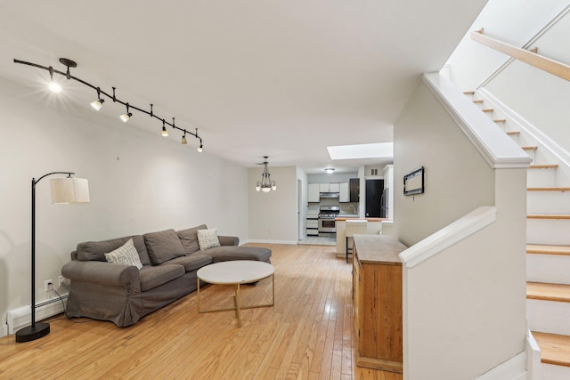 living room with a skylight, stairway, baseboards, a chandelier, and light wood-style floors