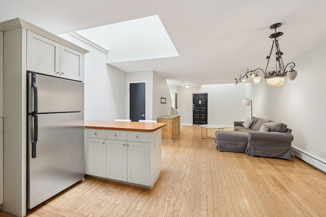 kitchen featuring butcher block countertops, open floor plan, stainless steel fridge, light wood-type flooring, and a skylight