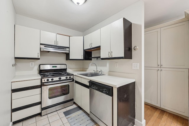 kitchen with appliances with stainless steel finishes, a sink, light countertops, light wood-style flooring, and under cabinet range hood