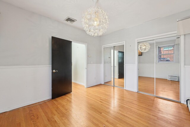 unfurnished bedroom with visible vents, light wood-style flooring, multiple closets, and a notable chandelier