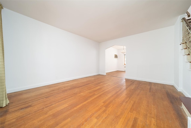 spare room featuring arched walkways, baseboards, light wood finished floors, and a chandelier