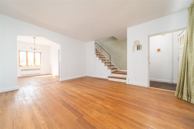 unfurnished living room featuring stairway, a chandelier, light wood-style flooring, and radiator