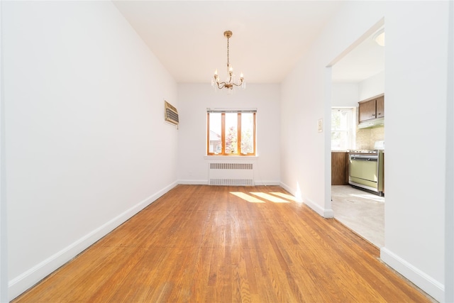 unfurnished dining area featuring baseboards, an inviting chandelier, light wood-style flooring, and radiator