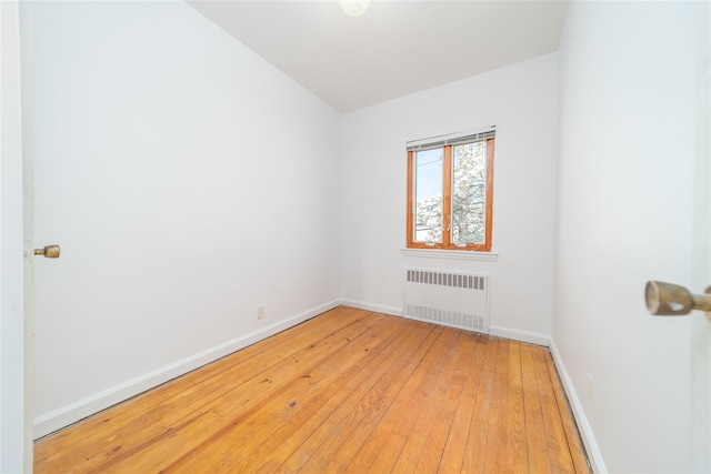 unfurnished room featuring radiator heating unit, baseboards, and light wood-type flooring