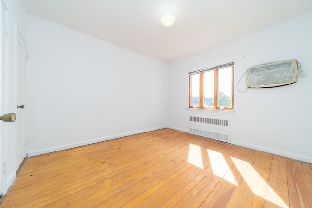 spare room featuring baseboards, radiator, and light wood-type flooring