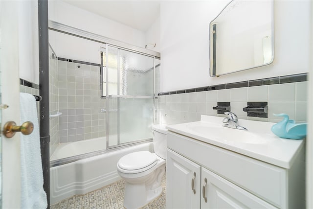 bathroom featuring vanity, toilet, tile walls, a wainscoted wall, and enclosed tub / shower combo