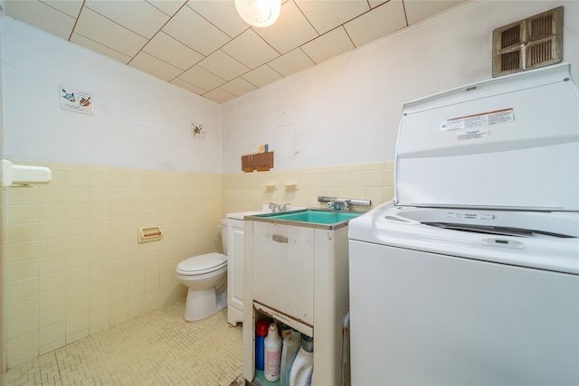 bathroom with tile patterned flooring, stacked washer and clothes dryer, wainscoting, toilet, and tile walls