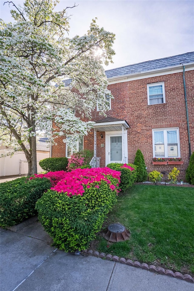 townhome / multi-family property with a high end roof, a front yard, and brick siding