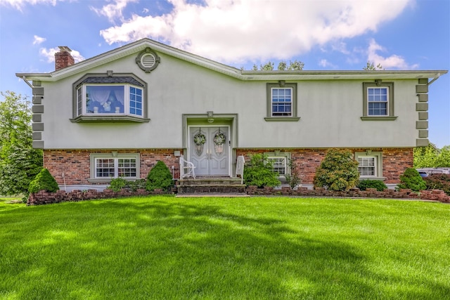 split foyer home featuring brick siding, stucco siding, a front yard, and a chimney